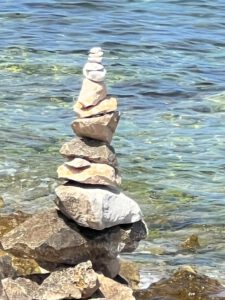 Zu sehen ist das Meer mit einem Kiesstrand und zu einem Turm gestapelte Steine